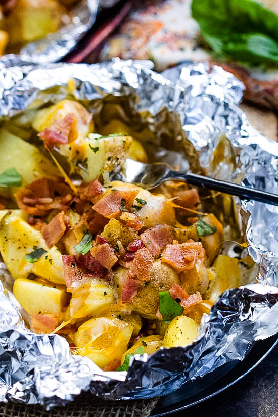 These easy Campfire Potato Foil Packs are flavorful, loaded potatoes cooked inside foil packs, then topped with melty cheese and bacon. This quick, delicious, and nourishing side dish recipe is great while camping or in the oven for any occasion! No pans to wash afterward makes the cook happy too!
